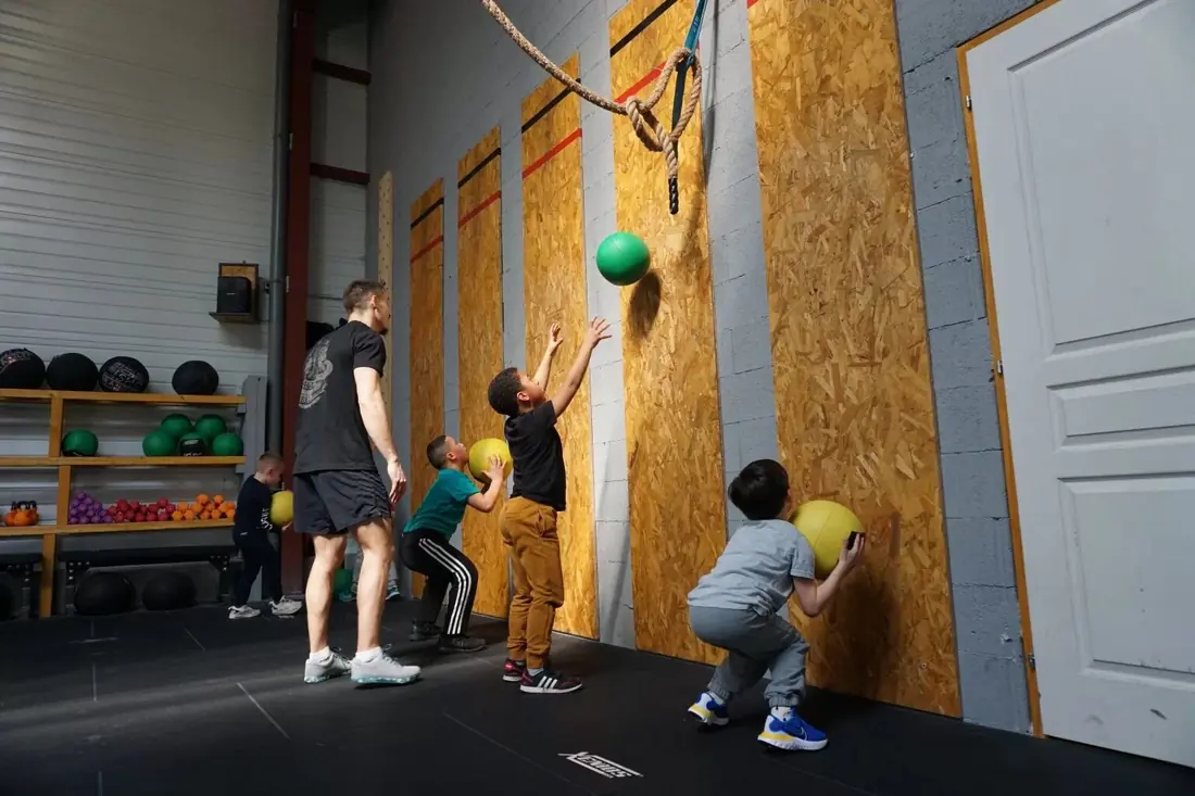 Enfants qui lancent des balles contre le mur, encadrés par un coach